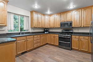 Kitchen featuring stainless steel appliances, dark stone countertops, light wood-style flooring, and light brown cabinets