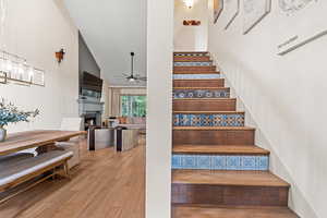 Staircase featuring a fireplace, wood finished floors, a ceiling fan, and high vaulted ceiling