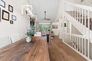 Dining area featuring a ceiling fan, wood finished floors, stairway, and high vaulted ceiling
