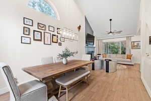 Dining space with high vaulted ceiling, light wood finished floors, a fireplace, ceiling fan, and a chandelier
