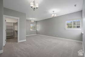 Unfurnished bedroom featuring a chandelier, light colored carpet, and a walk in closet