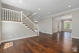 Unfurnished living room with stairway, dark wood finished floors, recessed lighting, ornamental molding, and a chandelier