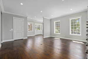 Unfurnished semi-formal living room/piano room/library featuring dark wood-type flooring, ornamental molding, and hanging lights