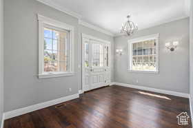 Foyer entrance with ornamental molding, dark wood finished floors, and a chandelier