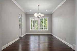 Unfurnished formal dining room with crown molding, chandelier, dark floors, and healthy amount of natural light
