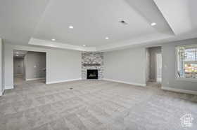 Unfurnished living room with a raised ceiling, light carpet, a large fireplace, and recessed lighting