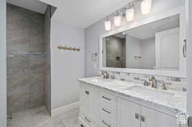 Full bathroom featuring walk in shower, double vanity, light tile patterned floors, and tasteful backsplash