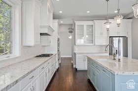Kitchen featuring healthy amount of natural light, light stone countertops, glass insert cabinets, white cabinetry, and recessed lighting