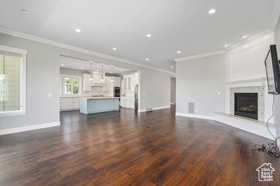 Unfurnished living room featuring crown molding, a fireplace with raised hearth, dark wood-style floors, and recessed lighting