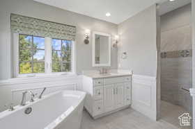 Bathroom featuring vanity, a freestanding tub, a walk in shower, a wainscoted wall, and a decorative wall