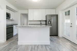 Kitchen with stainless steel appliances, white cabinets, light stone counters, and light wood-type flooring