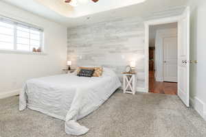 Bedroom featuring an accent wall, wooden walls, carpet flooring, a ceiling fan, and a raised ceiling