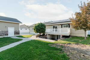 Back of house featuring a lawn, roof mounted solar panels, a wooden deck, and a patio area