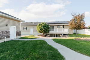 Back of property featuring a lawn, solar panels, a wooden deck, and stone siding