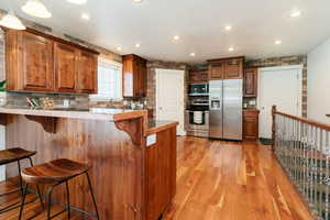 Kitchen featuring stainless steel appliances, a kitchen breakfast bar, tasteful backsplash, light wood-style floors, and recessed lighting