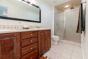 Full bathroom with a shower stall, light tile patterned flooring, double vanity, and backsplash