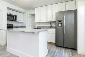 Kitchen with stainless steel appliances, light stone counters, white cabinetry, and light wood finished floors
