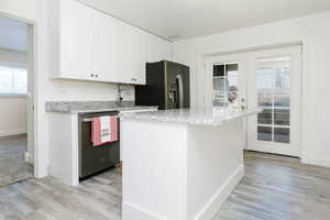 Kitchen with white cabinetry, stainless steel appliances, light stone countertops, and light wood finished floors