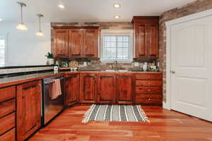 Kitchen featuring decorative light fixtures, stainless steel dishwasher, brown cabinets, light wood-style floors, and recessed lighting