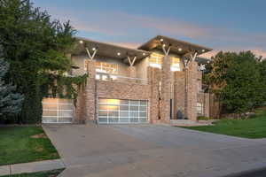 Modern home featuring a balcony, concrete driveway, stucco siding, a front yard, and stone siding