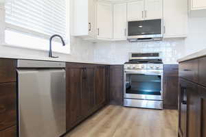 Kitchen with appliances with stainless steel finishes, white cabinetry, dark brown cabinets, decorative backsplash, and light wood-style floors