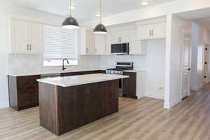 Kitchen featuring appliances with stainless steel finishes, white cabinets, pendant lighting, a kitchen island, and decorative backsplash