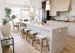 Kitchen with a breakfast bar area, hanging light fixtures, custom exhaust hood, light wood-style floors, and decorative backsplash