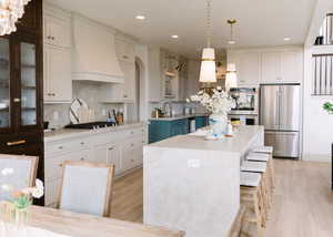 Kitchen with stainless steel appliances, a kitchen breakfast bar, a center island, decorative light fixtures, and custom range hood