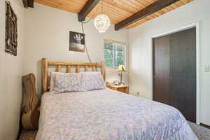 Bedroom featuring a wooden ceiling with exposed beams, a closet, a chandelier, and carpet