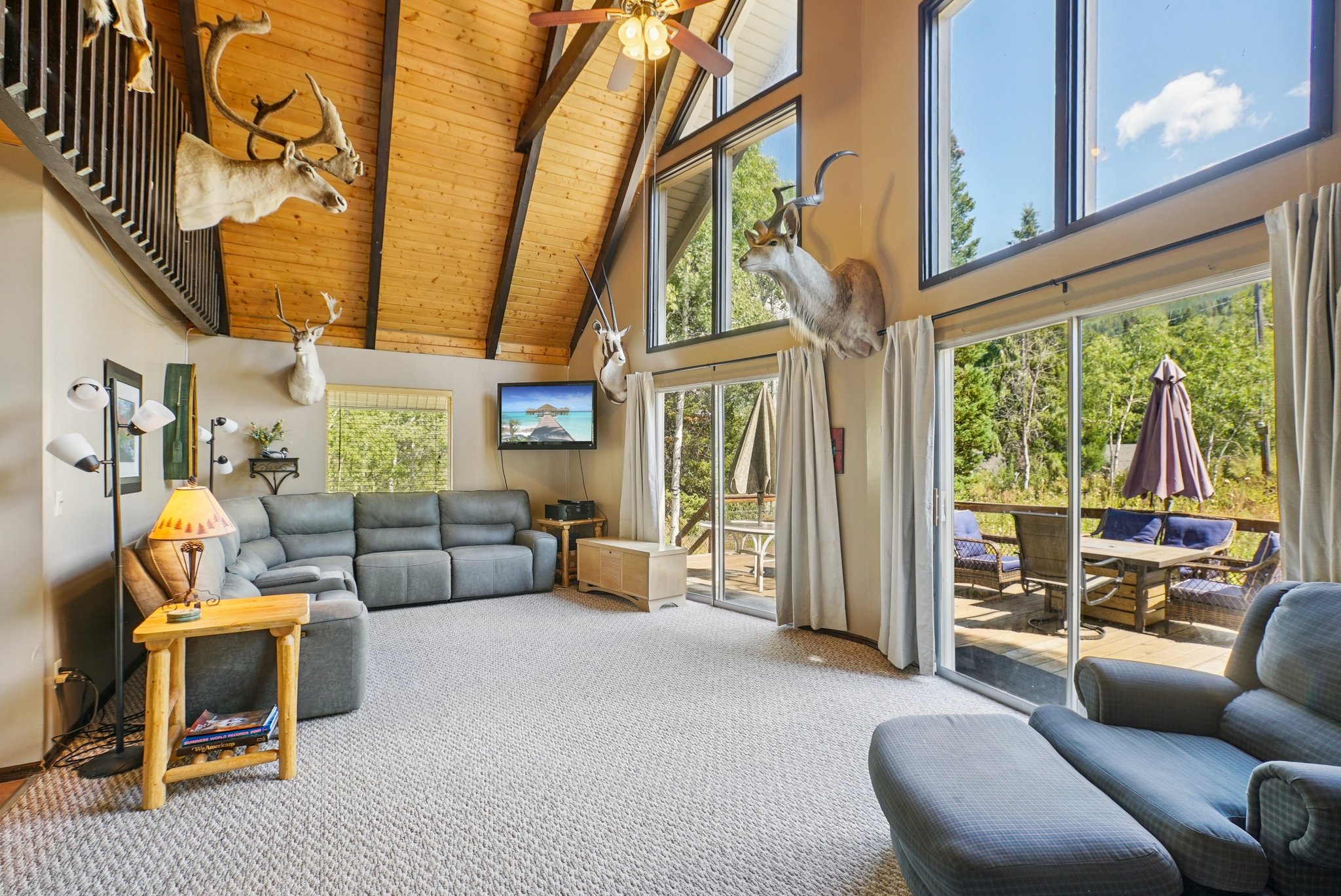 Carpeted living room with high vaulted ceiling, a wooden ceiling with exposed beams, and ceiling fan