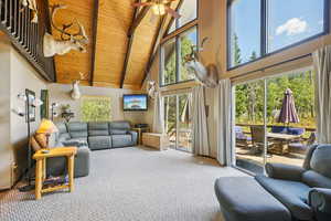 Carpeted living room with high vaulted ceiling, a wooden ceiling with exposed beams, and ceiling fan