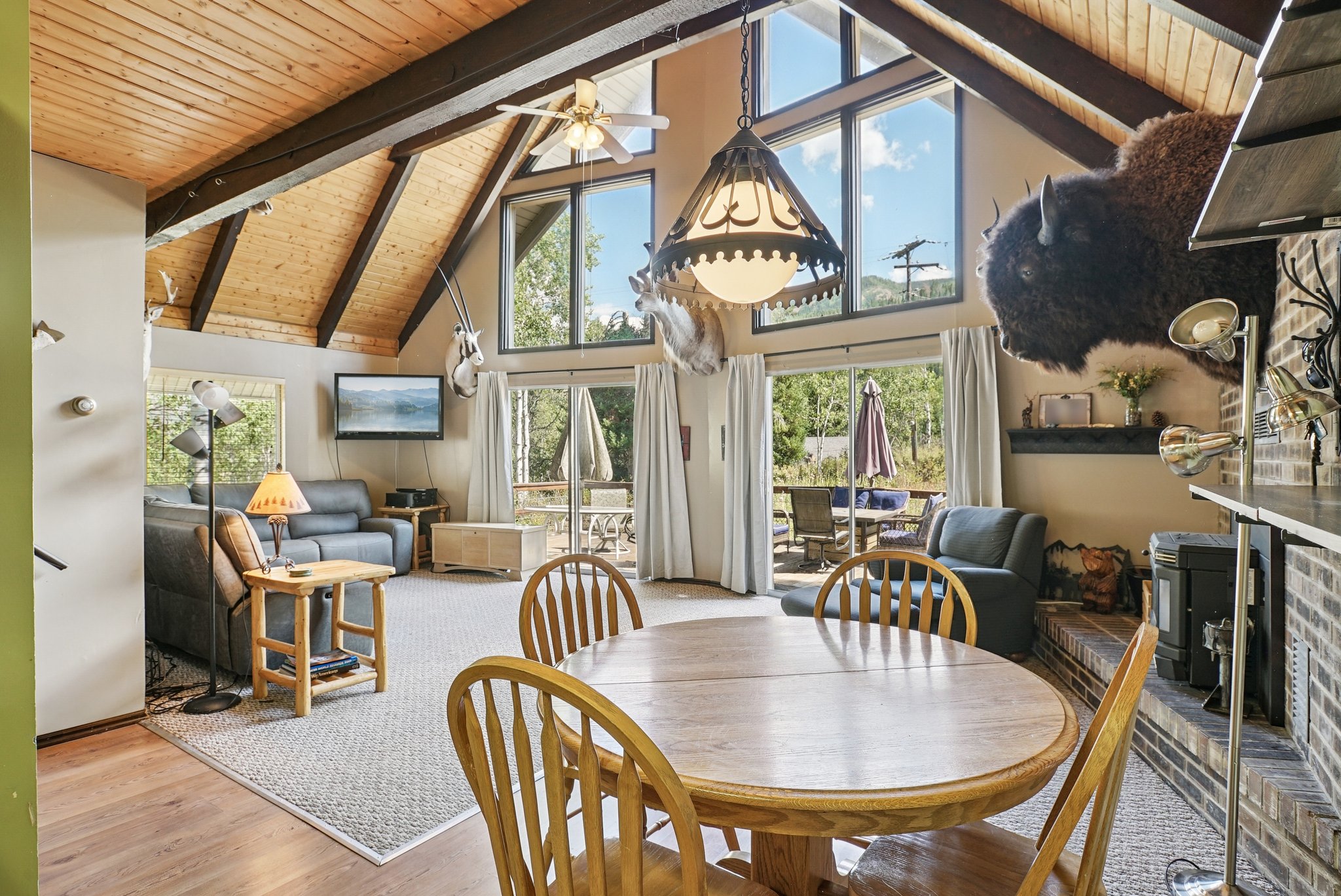 Dining area featuring a wooden ceiling with exposed beams, high vaulted ceiling, a wood stove, wood finished floors, and ceiling fan