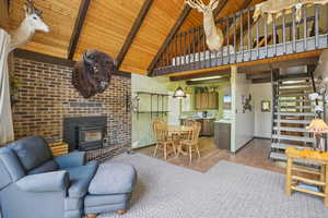 Living room featuring wood finished floors, a wood ceiling with exposed beams, a wood stove, brick wall, and high vaulted ceiling