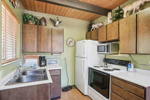Kitchen featuring white appliances, light wood-type flooring, light countertops, a wood ceiling with exposed beams, and brown cabinetry