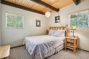 Carpeted bedroom with a wood ceiling with exposed beams and a chandelier