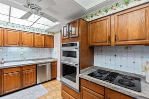 Kitchen featuring decorative backsplash, brown cabinets, stainless steel appliances, and ceiling fan
