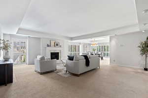 Living area featuring light carpet, a fireplace, a chandelier, and a raised ceiling