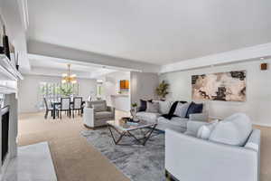 Living room with a fireplace with flush hearth, a tray ceiling, carpet flooring, a chandelier, and ornamental molding
