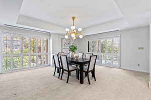 Dining area with a raised ceiling, light carpet, and a chandelier