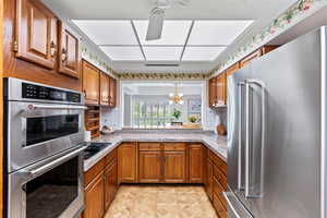 Kitchen with brown cabinets, stainless steel appliances, a chandelier, light countertops, and backsplash