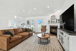 Living area featuring arched walkways, plenty of natural light, a glass covered fireplace, recessed lighting, and light wood-style flooring