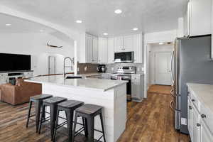 Kitchen featuring open floor plan, appliances with stainless steel finishes, arched walkways, a kitchen breakfast bar