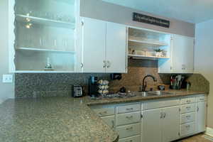 Kitchen with open shelves, decorative backsplash, white cabinetry,