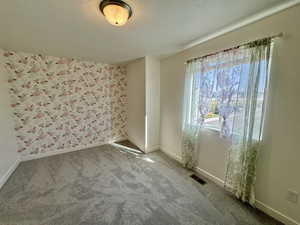 Carpeted spare room featuring wallpapered walls and a textured ceiling