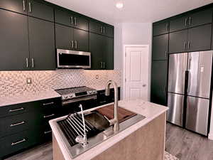 Kitchen featuring dark cabinetry, appliances with stainless steel finishes, light stone counters, a textured ceiling, and backsplash