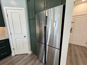 Kitchen featuring green cabinetry, stainless steel fridge, light wood finished floors, backsplash, and light countertops