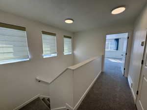 Hallway featuring dark colored carpet and an upstairs landing