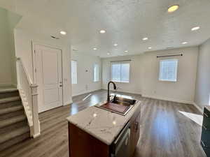 Kitchen featuring an island with sink, a textured ceiling, open floor plan, light wood-style floors, and recessed lighting