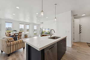 Kitchen with pendant lighting, a center island with sink, dishwasher, light wood-type flooring, and open floor plan
