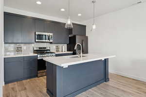 Kitchen featuring appliances with stainless steel finishes, pendant lighting, a center island with sink, tasteful backsplash, and modern cabinets